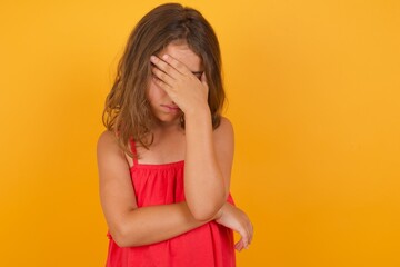 Caucasian young girl standing against yellow background making facepalm gesture while smiling amazed with stupid situation.