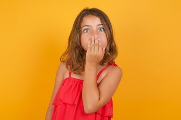 Oh! I think I said it! Close up portrait Caucasian young girl standing against yellow background cover open mouth by hand palm, look at camera with big eyes.