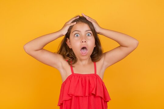 Horrible, stress, shock. Portrait emotional crazy young Caucasian girl standing against yellow background clasping head in hands. Emotions, facial expression concept.