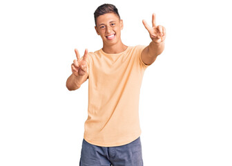 Young handsome man wearing casual clothes smiling with tongue out showing fingers of both hands doing victory sign. number two.