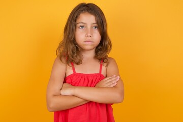 Picture of angry young Caucasian girl standing against yellow background looking camera.