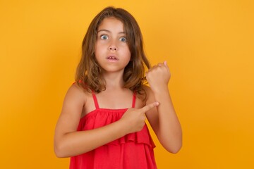 young Caucasian girl standing against yellow background in hurry pointing to watch time, impatience, upset and angry for deadline delay