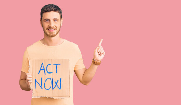 Handsome young man with bear holding act now banner surprised with an idea or question pointing finger with happy face, number one