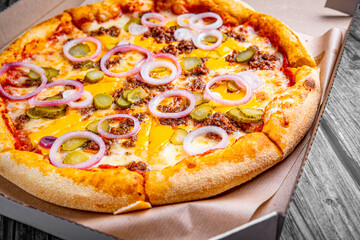 Pizza with Mozzarella cheese, Bolognese sauce, minced meat and vegetables. Italian pizza in paper box on wooden background.