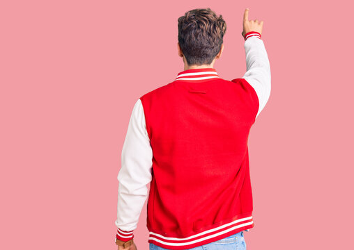 Young handsome man wearing baseball uniform posing backwards pointing ahead with finger hand