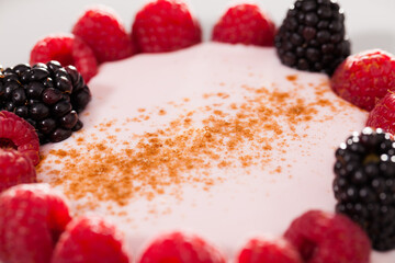 raspberries and blackberries laid out on a white plate in circle with yogurt and cinnamon