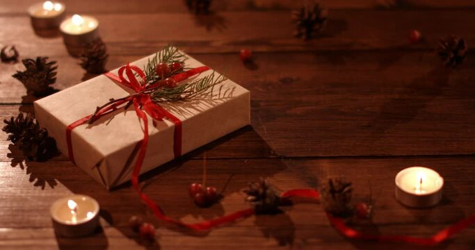 A flat gift box tied with a red ribbon and burning candles on a wooden table