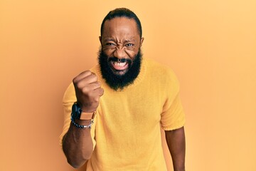 Obraz premium Young african american man wearing casual clothes angry and mad raising fist frustrated and furious while shouting with anger. rage and aggressive concept.