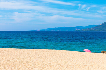 Fototapeta na wymiar Empty sandy beach and pink parasol with mountain in the background, Beach of Propriano, Corsica, France. Place for Text