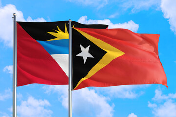 East Timor and Antigua and Barbuda national flag waving in the windy deep blue sky. Diplomacy and international relations concept.