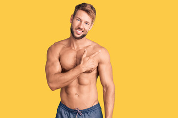 Young caucasian man standing shirtless cheerful with a smile of face pointing with hand and finger up to the side with happy and natural expression on face