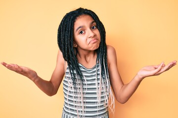 Young african american girl child with braids over yellow background clueless and confused...