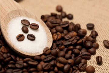 coffee beans with sugar in wooden spoon,
raffia fabric background