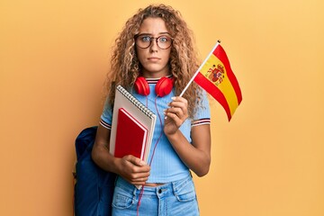 Beautiful caucasian teenager girl exchange student holding spanish flag skeptic and nervous,...