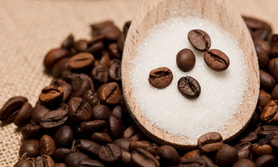 coffee beans with sugar in wooden spoon,
raffia fabric background