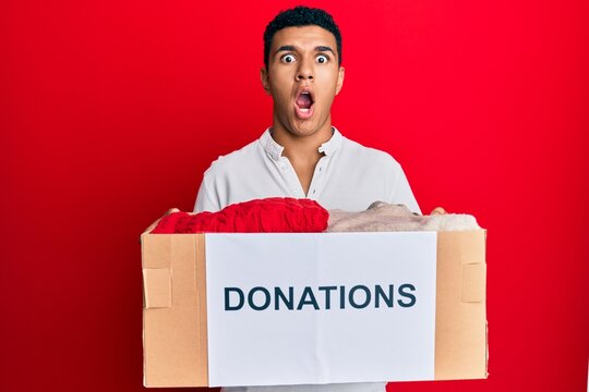 Young arab man holding donation box with clothes afraid and shocked with surprise and amazed expression, fear and excited face.