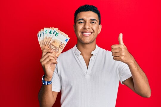 Young arab man holding 50 euro banknotes smiling happy and positive, thumb up doing excellent and approval sign