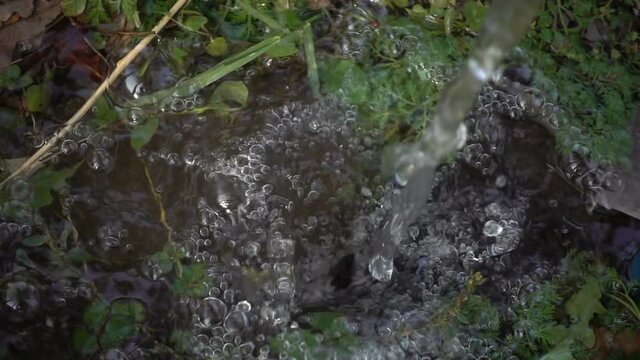 Closeup splashing water in slow motion. Stream of water falling on green grass.