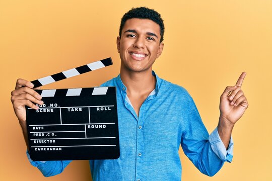 Young arab man holding video film clapboard smiling happy pointing with hand and finger to the side