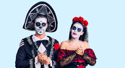 Young couple wearing mexican day of the dead costume over background with hands together and crossed fingers smiling relaxed and cheerful. success and optimistic