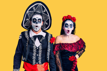 Young couple wearing mexican day of the dead costume over background afraid and shocked with surprise and amazed expression, fear and excited face.