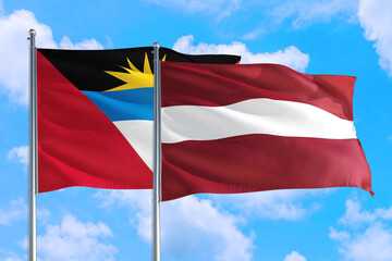 Latvia and Antigua and Barbuda national flag waving in the windy deep blue sky. Diplomacy and international relations concept.