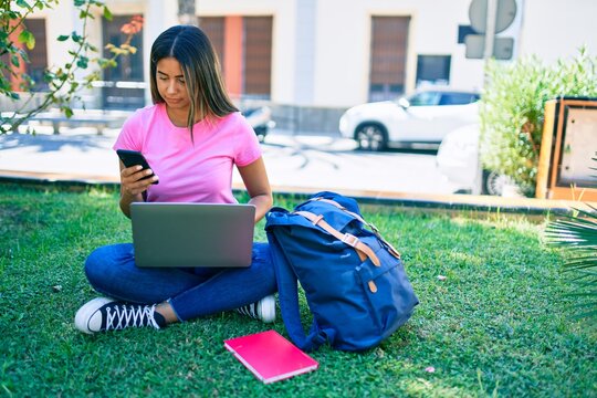 Young latin student girl smiling happy using smartphone and laptop at university campus.