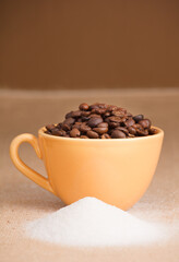 coffee beans in yellow cup with sugar, on raffia cloth and brown background