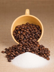 coffee beans in yellow cup with sugar, on raffia cloth and brown background
