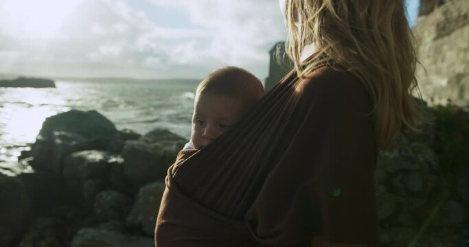 A young mother is standing on the coast with her baby in a sling in the autumn