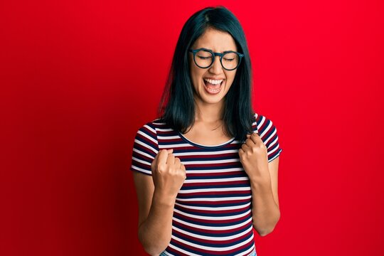 Beautiful asian young woman wearing casual clothes and glasses celebrating surprised and amazed for success with arms raised and eyes closed