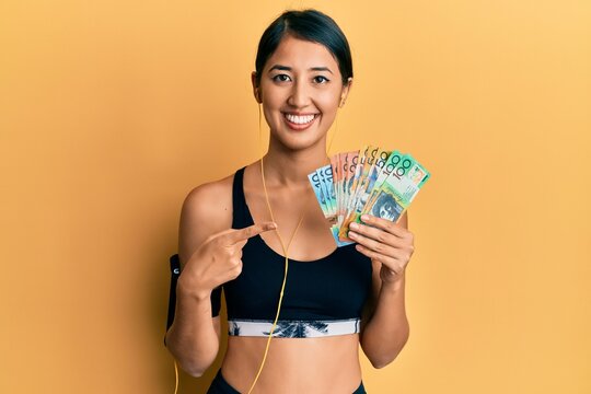 Beautiful asian young sport woman holding australian dollars smiling happy pointing with hand and finger