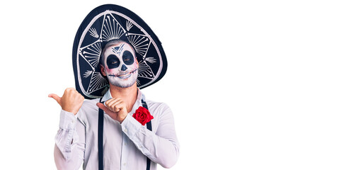 Man wearing day of the dead costume over background pointing to the back behind with hand and thumbs up, smiling confident
