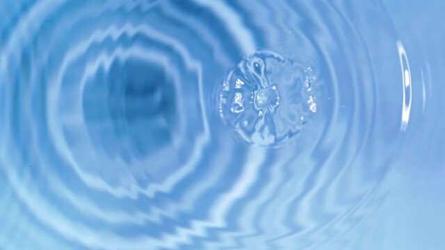 Top view slow motion of drop falling into the water surface and diverging circles on white background