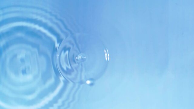 Top view slow motion of drop falling into the water surface and diverging circles on white background