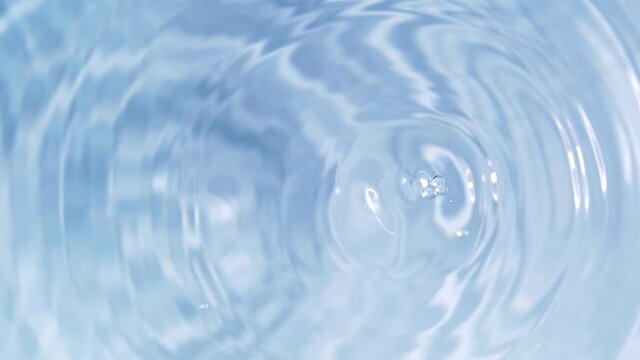 Top view slow motion of drop falling into the water surface and diverging circles on white background