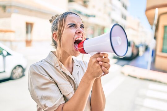 Young beautiful blonde caucasian woman smiling happy outdoors on a sunny day shouting through megaphone