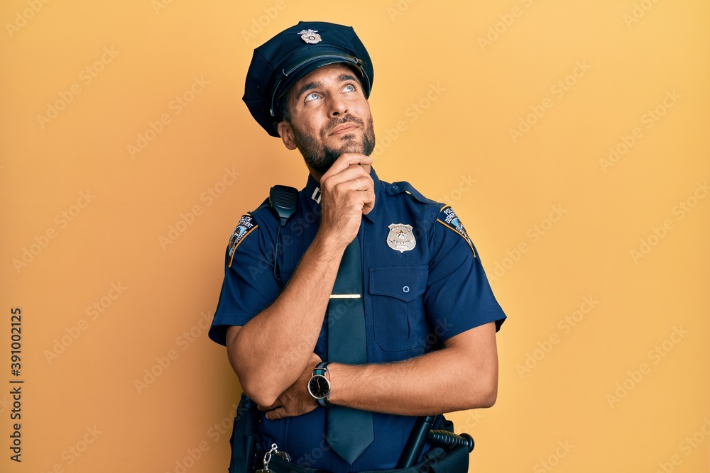 Sticker Handsome hispanic man wearing police uniform with hand on chin thinking about question, pensive expression. smiling and thoughtful face. doubt concept.