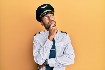 Handsome hispanic man wearing airplane pilot uniform with hand on chin thinking about question, pensive expression. smiling with thoughtful face. doubt concept. © Krakenimages.com