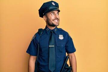 Handsome hispanic man wearing police uniform looking away to side with smile on face, natural expression. laughing confident.