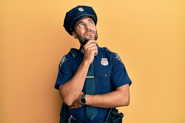Handsome hispanic man wearing police uniform with hand on chin thinking about question, pensive...