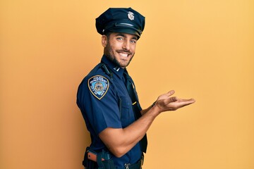 Handsome hispanic man wearing police uniform pointing aside with hands open palms showing copy...