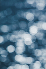 Glittering silver bokeh on surface of blue water.