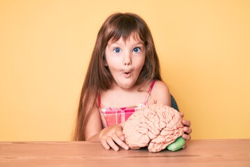 Little caucasian kid girl with long hair holding brain as mental health concept scared and amazed...