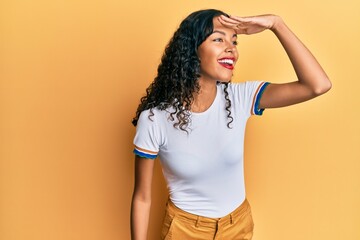 Young african american girl wearing casual clothes very happy and smiling looking far away with hand over head. searching concept.