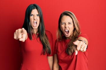 Hispanic family of mother and daughter wearing casual clothes over red background pointing displeased and frustrated to the camera, angry and furious with you