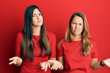 Hispanic family of mother and daughter wearing casual clothes over red background clueless and confused with open arms, no idea concept.