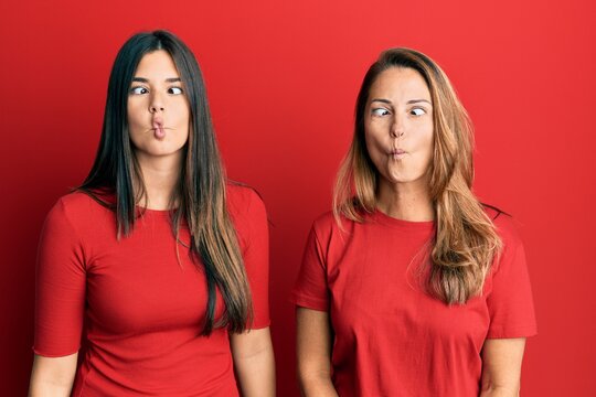 Hispanic family of mother and daughter wearing casual clothes over red background making fish face with lips, crazy and comical gesture. funny expression.