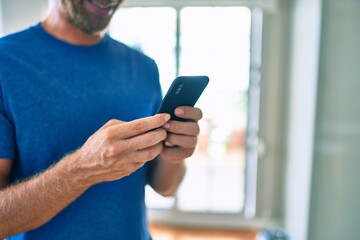Young irish man smiling happy using smartphone standing at home.