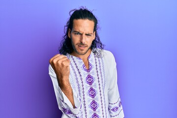 Fototapeta premium Young handsome man with long hair wearing bohemian and hippie shirt angry and mad raising fist frustrated and furious while shouting with anger. rage and aggressive concept.